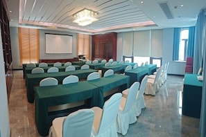 A conference room with rows of tables and chairs, a projector screen, and a large window. - Bainian Hotel (Hepu)