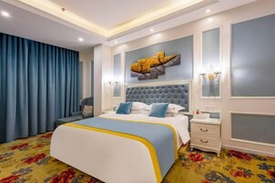 A hotel room with a large bed, a tufted headboard, a decorative wall piece, a nightstand, and a patterned carpet.