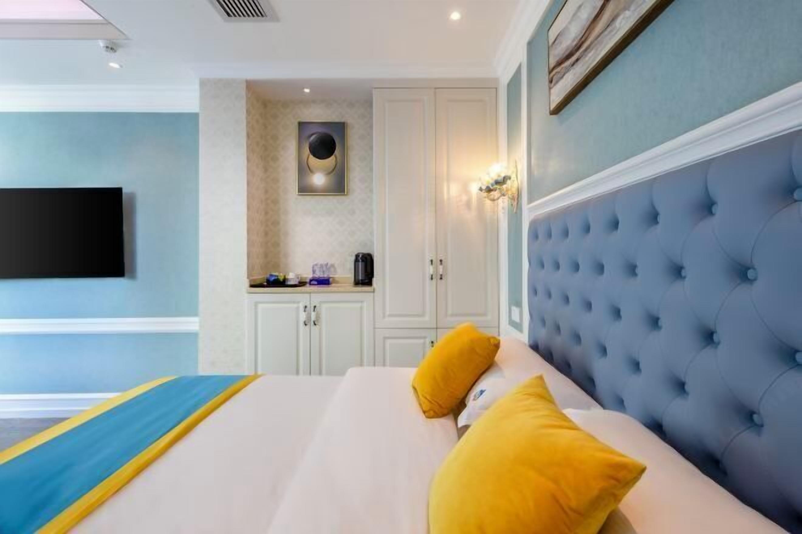Een moderne hotelkamer met een groot bed, een flatscreen televisie aan de wand, een klein kitchenette en een gestoffeerd hoofdeinde.