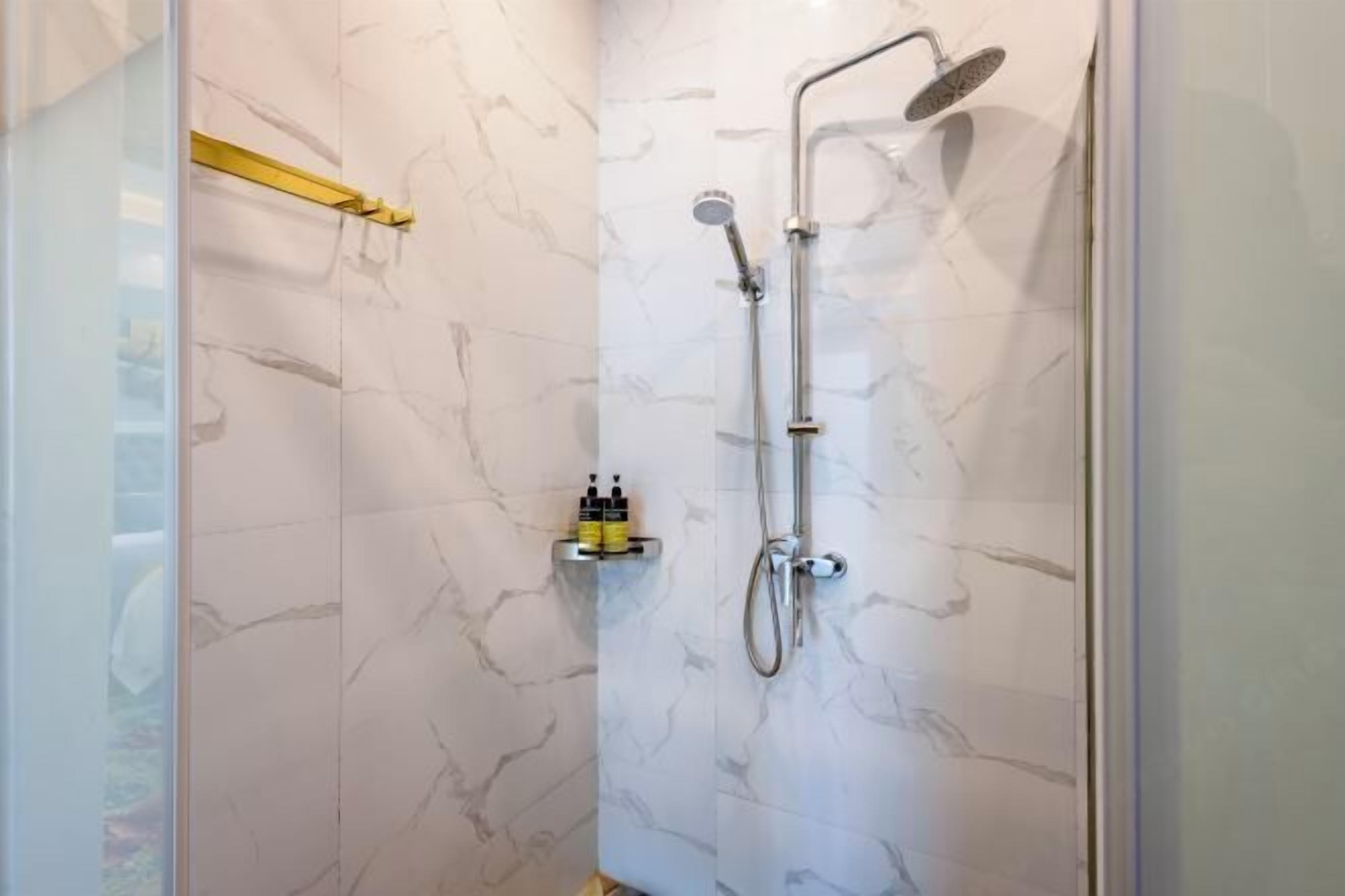 A shower with a handheld showerhead and a wall-mounted faucet, marble-patterned walls, and a yellow towel rack.