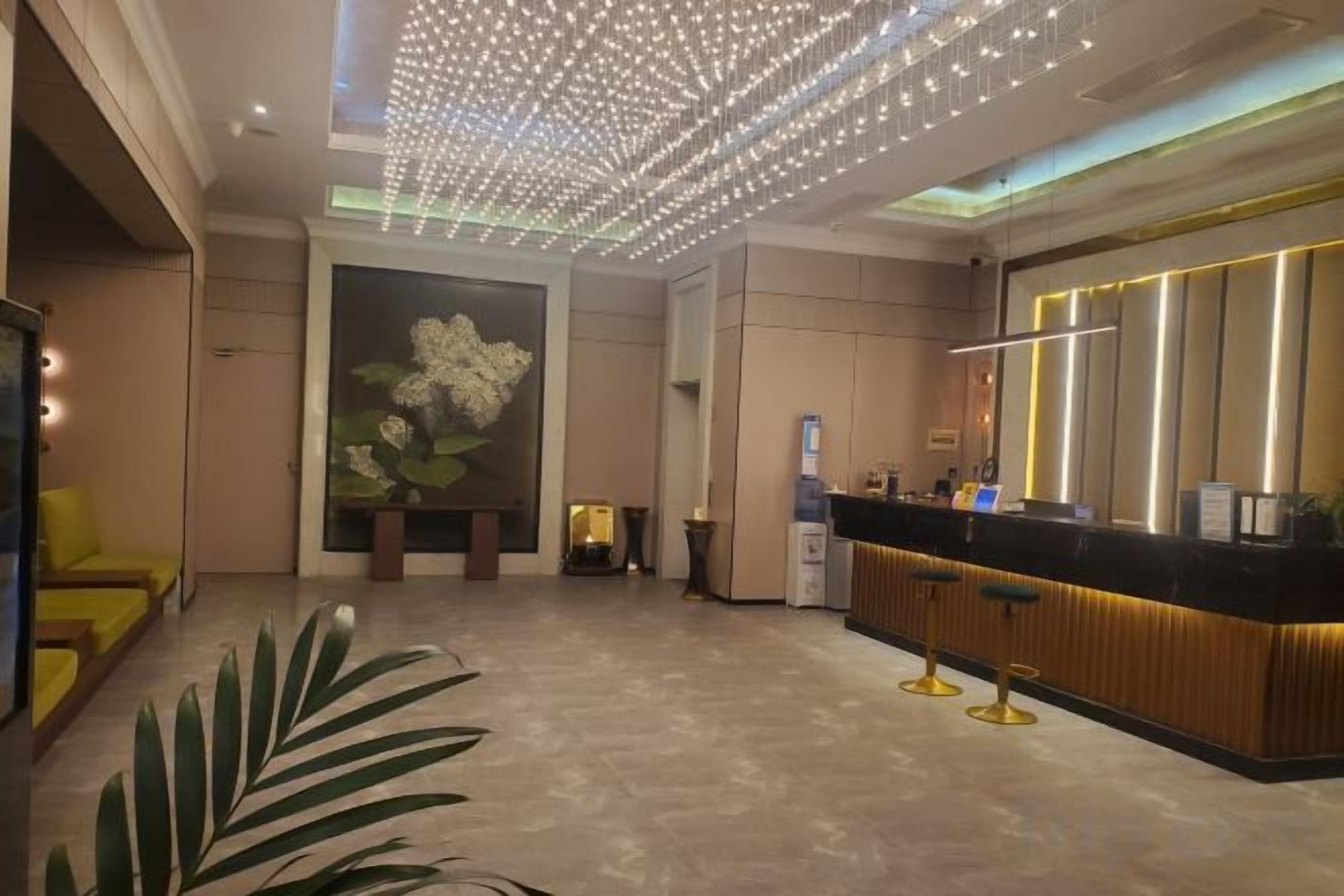 A hotel lobby with a reception desk, seating area, and a large floral painting on the wall.