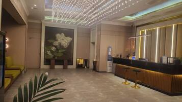A hotel lobby with a reception desk, seating area, and a large floral painting on the wall.