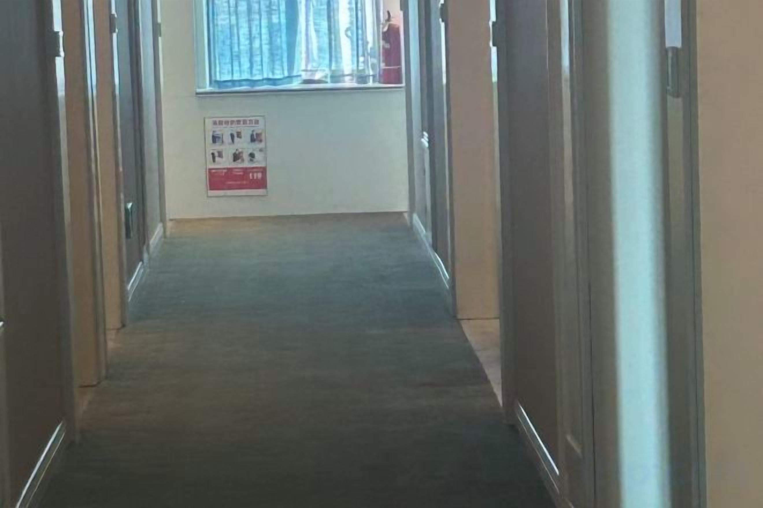 Un couloir dont le sol est recouvert d’une moquette, menant à une fenêtre offrant une vue.