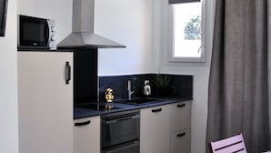 A compact kitchen with a microwave, stove, and sink, a small dining area with a chair and table, and a window with curtains. - Villa Ibanova 3: Studio, private parking (Collioure)
