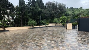 A courtyard with a tiled floor, surrounded by trees and a low wall. - Villa Ibanova 3: Studio, private parking (Collioure)