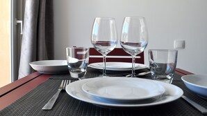 A table set with plates, glasses, and a bowl, with a view of a window and curtains in the background. - Villa Ibanova 3: Studio, private parking (Collioure)