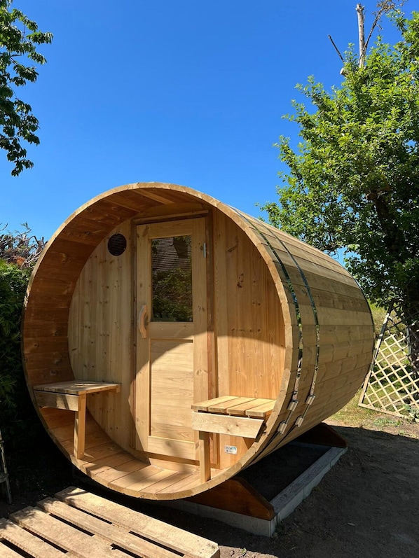 A wooden barrel-shaped structure with a door and two benches inside. - Vacation home in the middle of nature (Remplin)