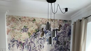 Un comedor con una mesa redonda de madera, cuatro sillas con cojines de cuadros y un mural floral en la pared.