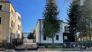 Zona residencial con un edificio blanco, una cerca negra y un árbol.