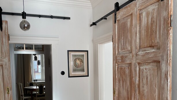 Un pasillo con suelo de madera, una puerta corrediza estilo granero, un cuadro en la pared y una zona de comedor al fondo.