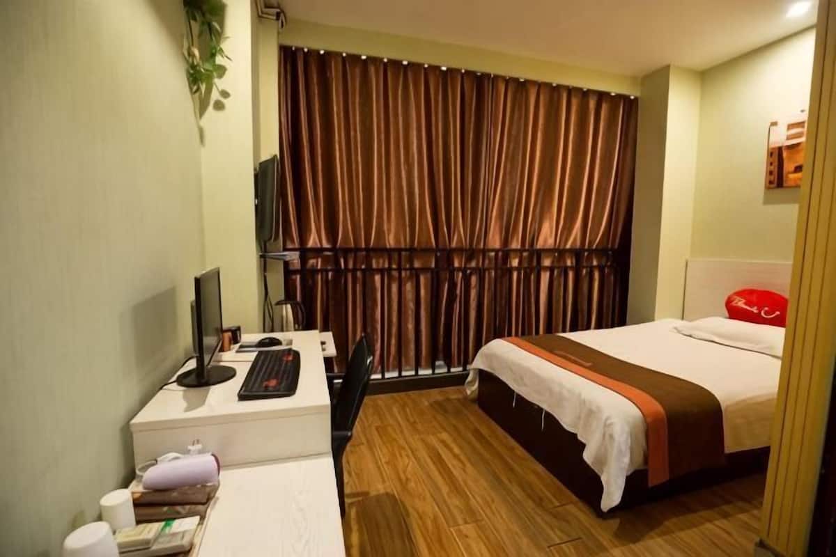 A hotel room with a bed, a desk with a computer, a TV, and a window with curtains.