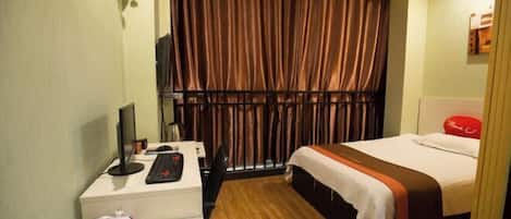 A hotel room with a desk, a bed, a TV, and a window with curtains.