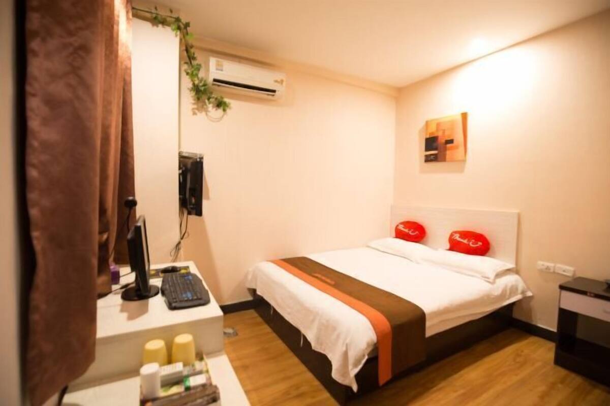 A hotel room with a bed, a desk with a computer, a chair, and a small table with toiletries.