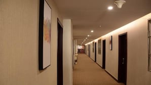 A long, narrow hotel corridor with doors on both sides, a carpeted floor, and framed artwork on the walls. - Shushi Hotel (Shiyan)