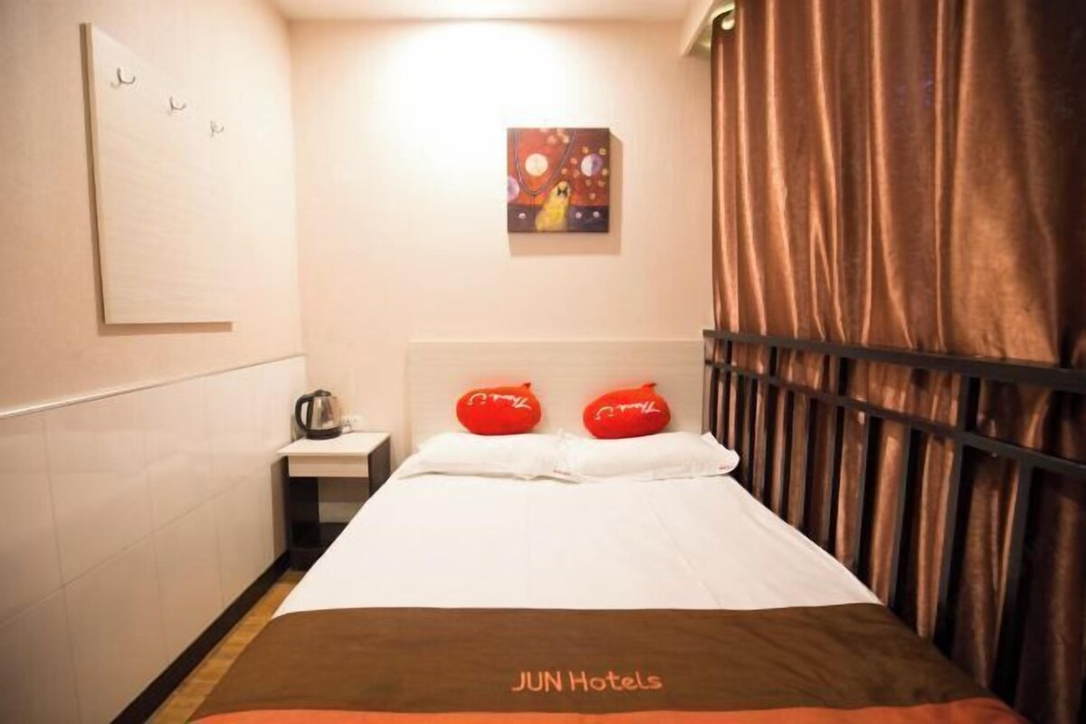 Una habitación de hotel con cama, mesita de noche, un cuadro en la pared y cortina.