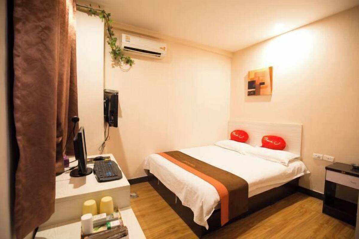 A hotel room with a bed, a desk with a computer, an air conditioner, and a wall-mounted artwork.