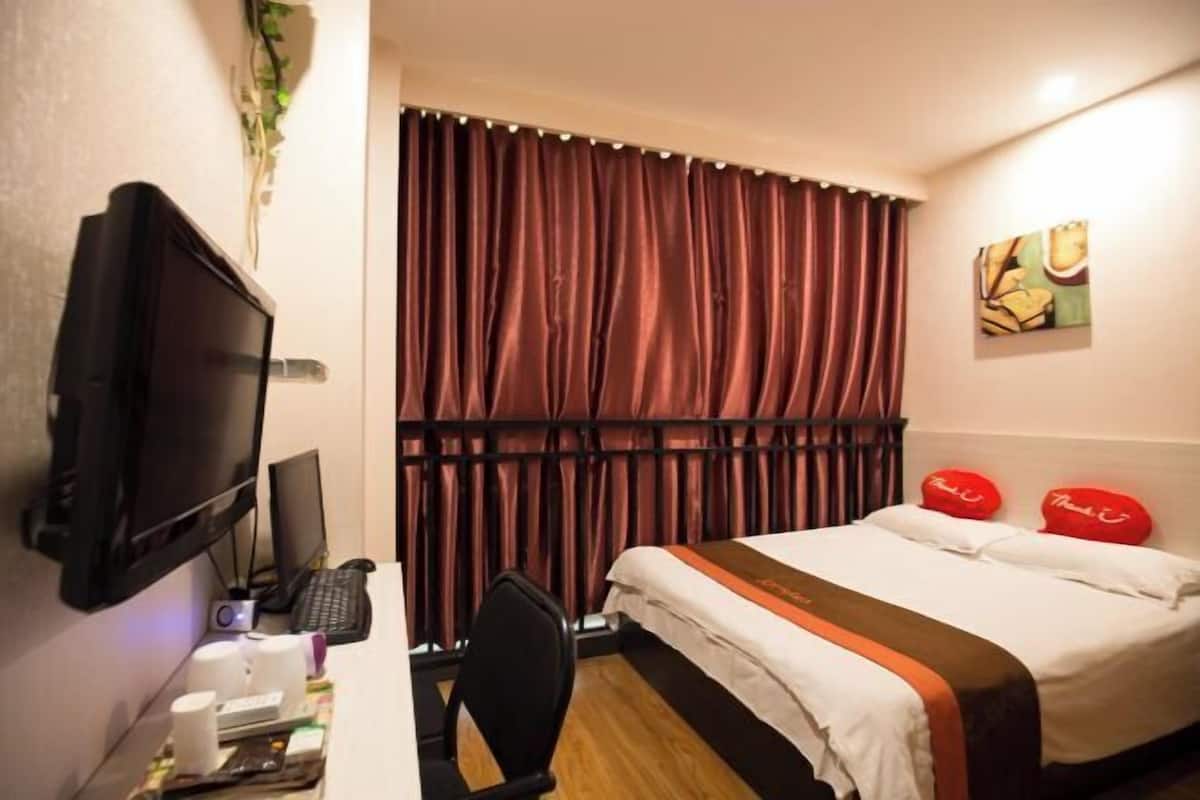 A hotel room with a bed, a desk with a computer, a television, and a window with curtains.