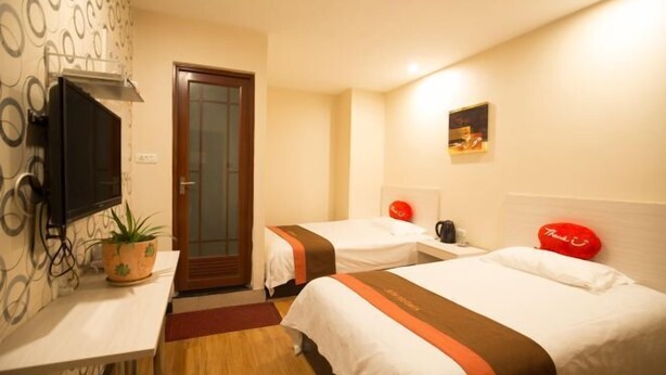 A hotel room with two beds, a TV, a small table, a potted plant, and a door. - Shushi Hotel (Shiyan)