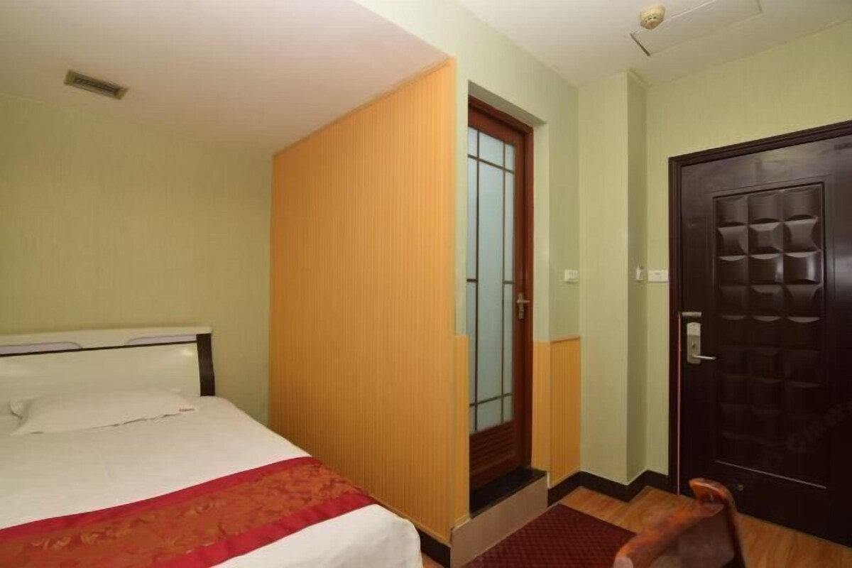 Una habitación de hotel con cama, un armario de madera, una puerta y una alfombra pequeña.
