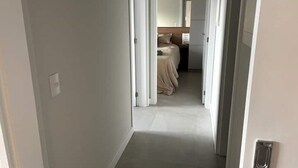 Un estrecho pasillo que lleva a un dormitorio con una cama y una mesita de noche pequeña.
