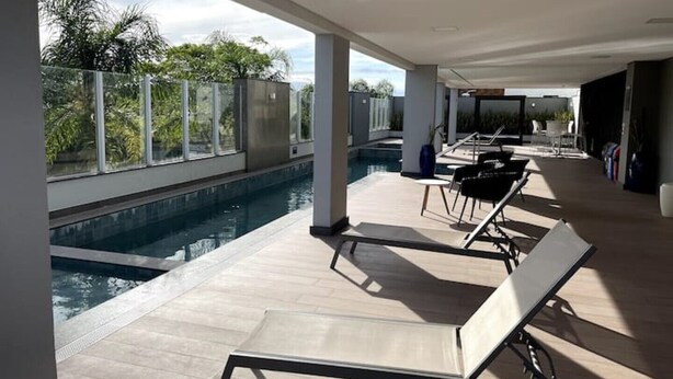 Un área de piscina moderna al aire libre con sillones de descanso y vistas al follaje circundante.