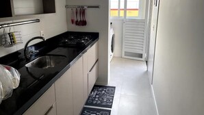 Cocina moderna con encimera negra, pileta de acero inoxidable y muebles blancos. Se ve una ventana con vistas a un edificio.