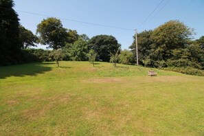 Un campo cubierto de hierba con un banco y árboles al fondo.