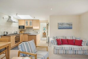 Un espacio habitable compacto con kitchenette, sofá a rayas con cojines rojos y una pintura de una escena costera.