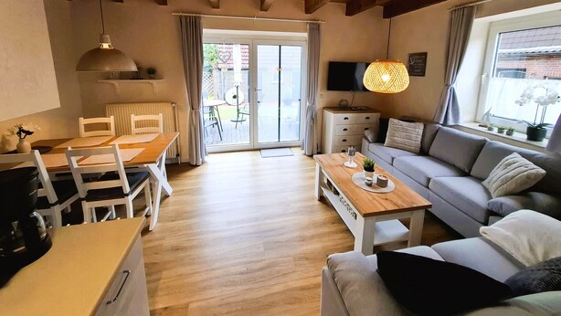 En hyggelig stue med træloft, spiseplads med bord og stole, en sofa og et fjernsyn på væggen.