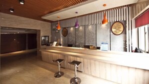 Un espace d’accueil doté d’un plafond en bois, d’un comptoir de réception, de deux tabourets de bar et de luminaires suspendus.