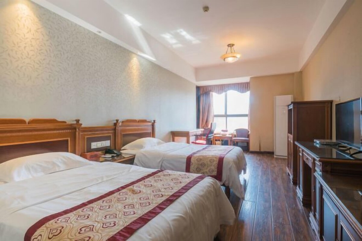 A hotel room with two beds, a desk, a chair, a television, and a window with curtains.