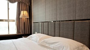 Une chambre d’hôtel avec un grand lit, une tête de lit dotée de panneaux verticaux, une lampe et une fenêtre avec des rideaux.