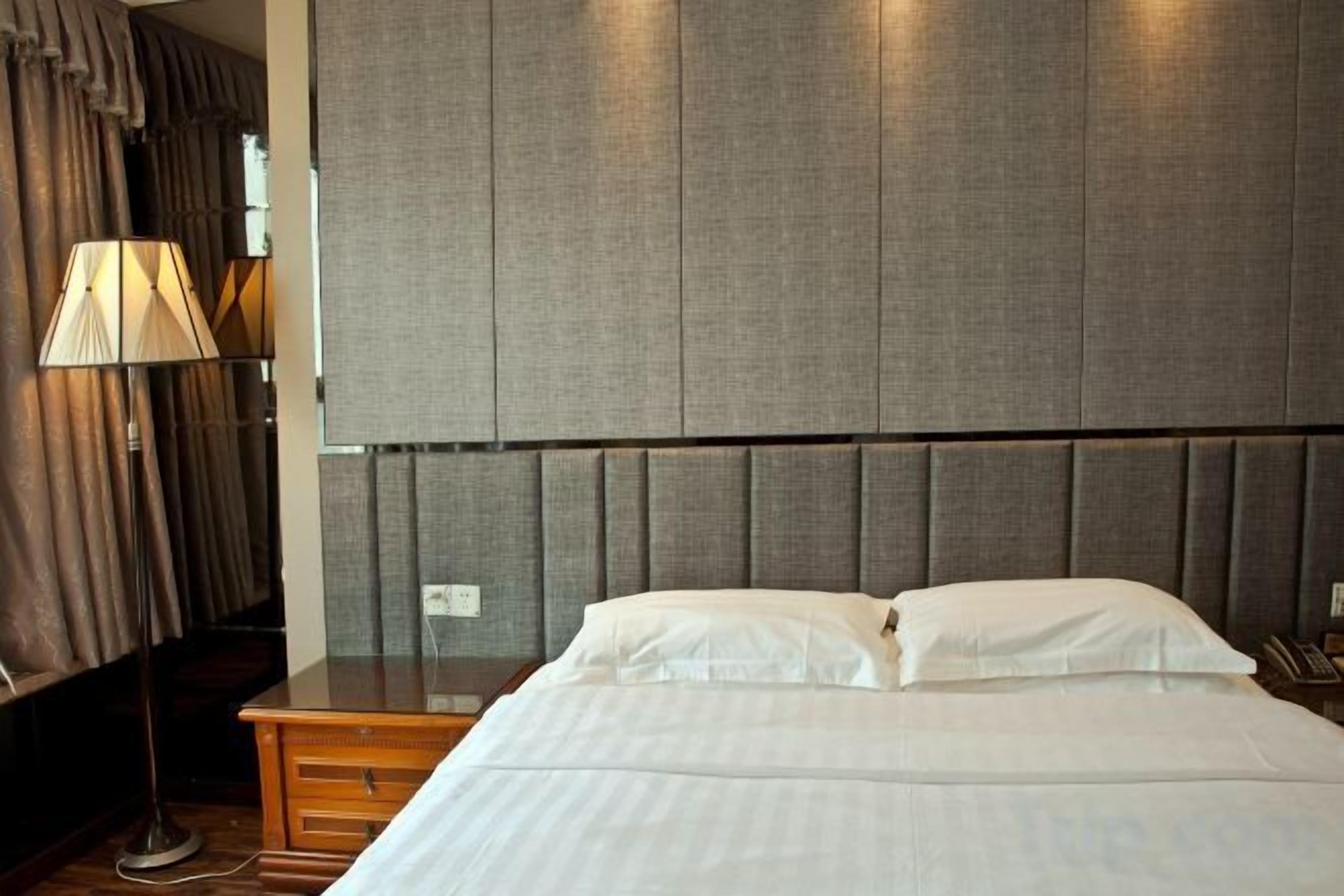 A hotel room with a bed, a nightstand, a lamp, and a headboard.