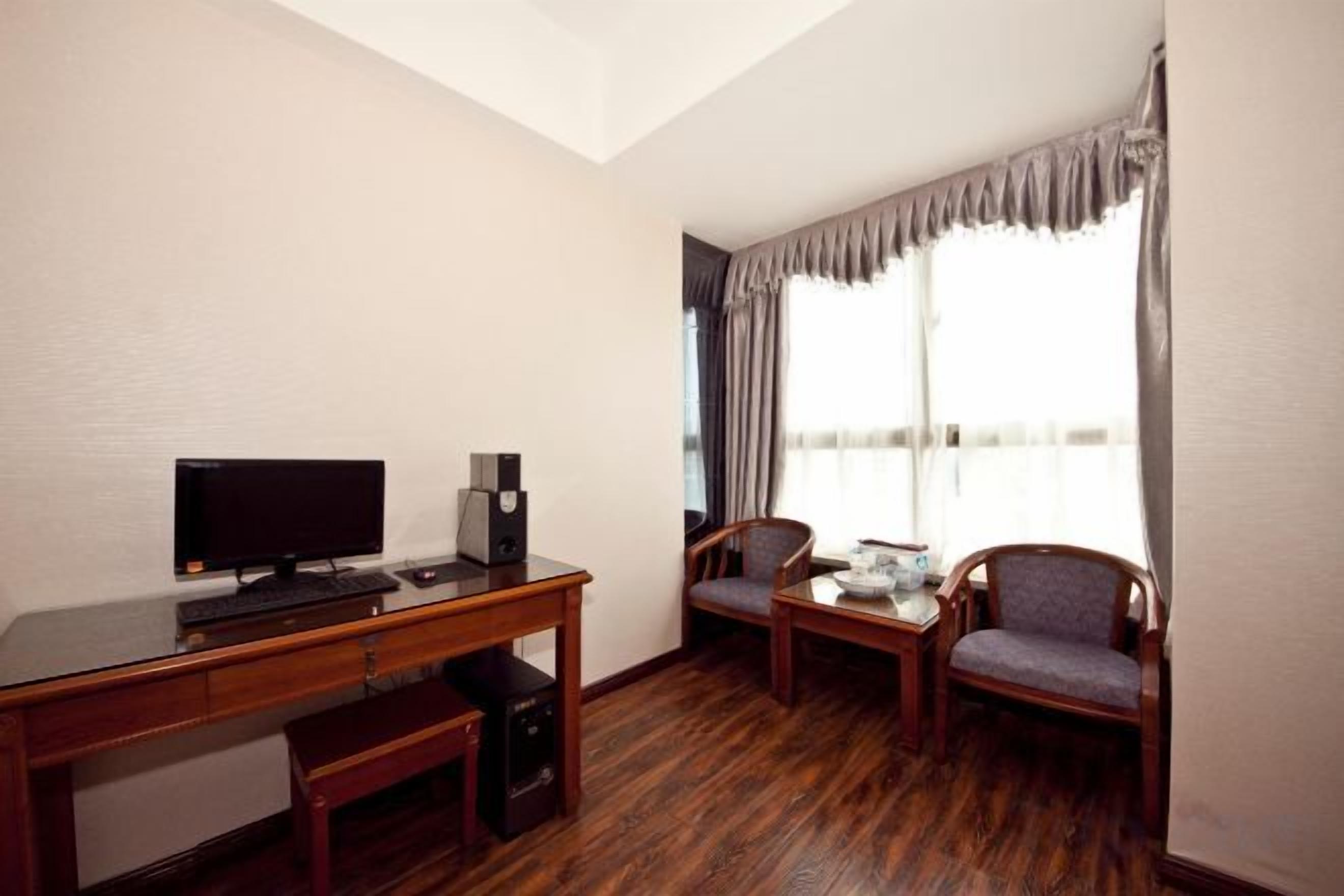 A hotel room with a desk, a television, a chair, and a window with curtains.