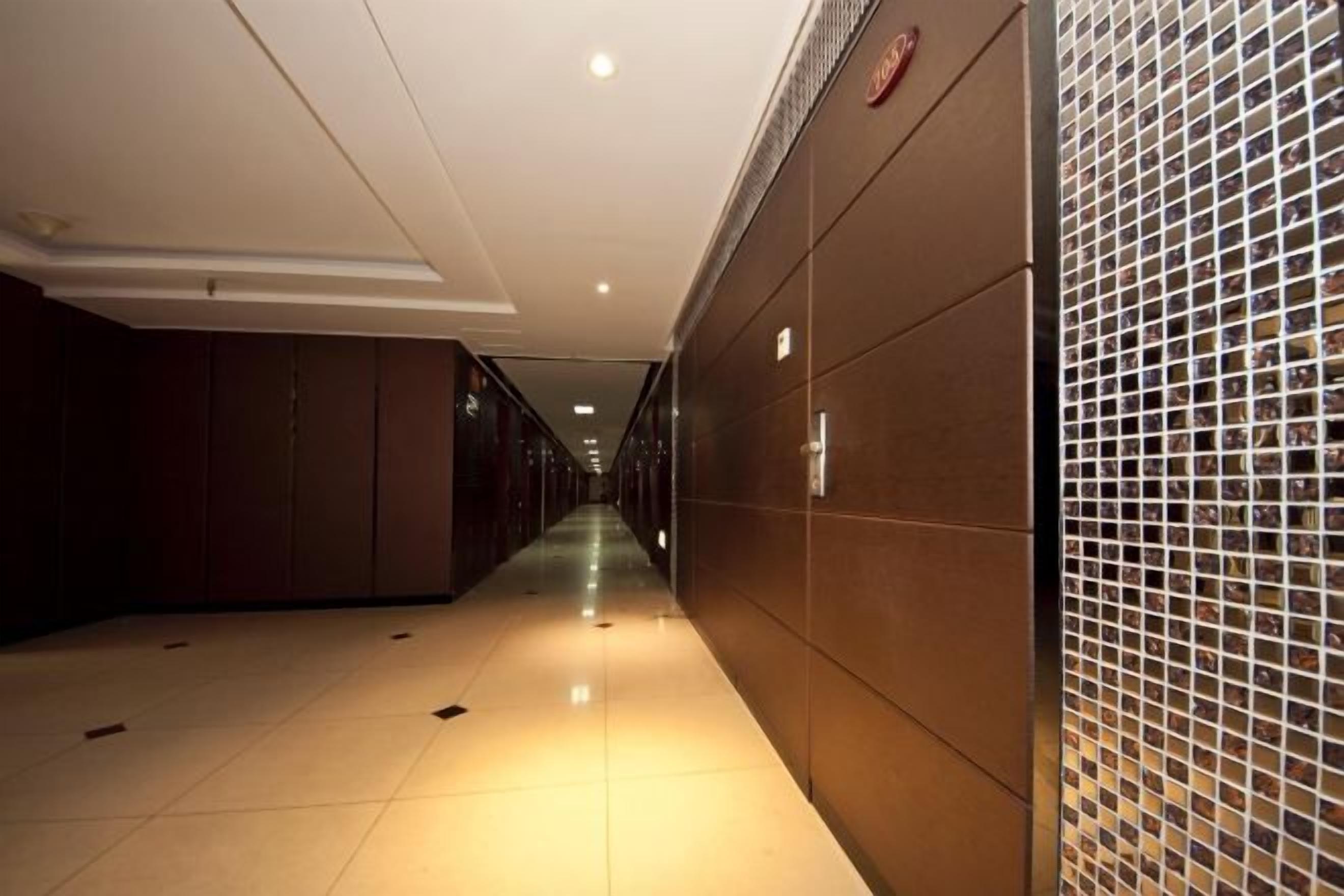 A hotel corridor with a long hallway, doors on one side, and a tiled wall on the other.
