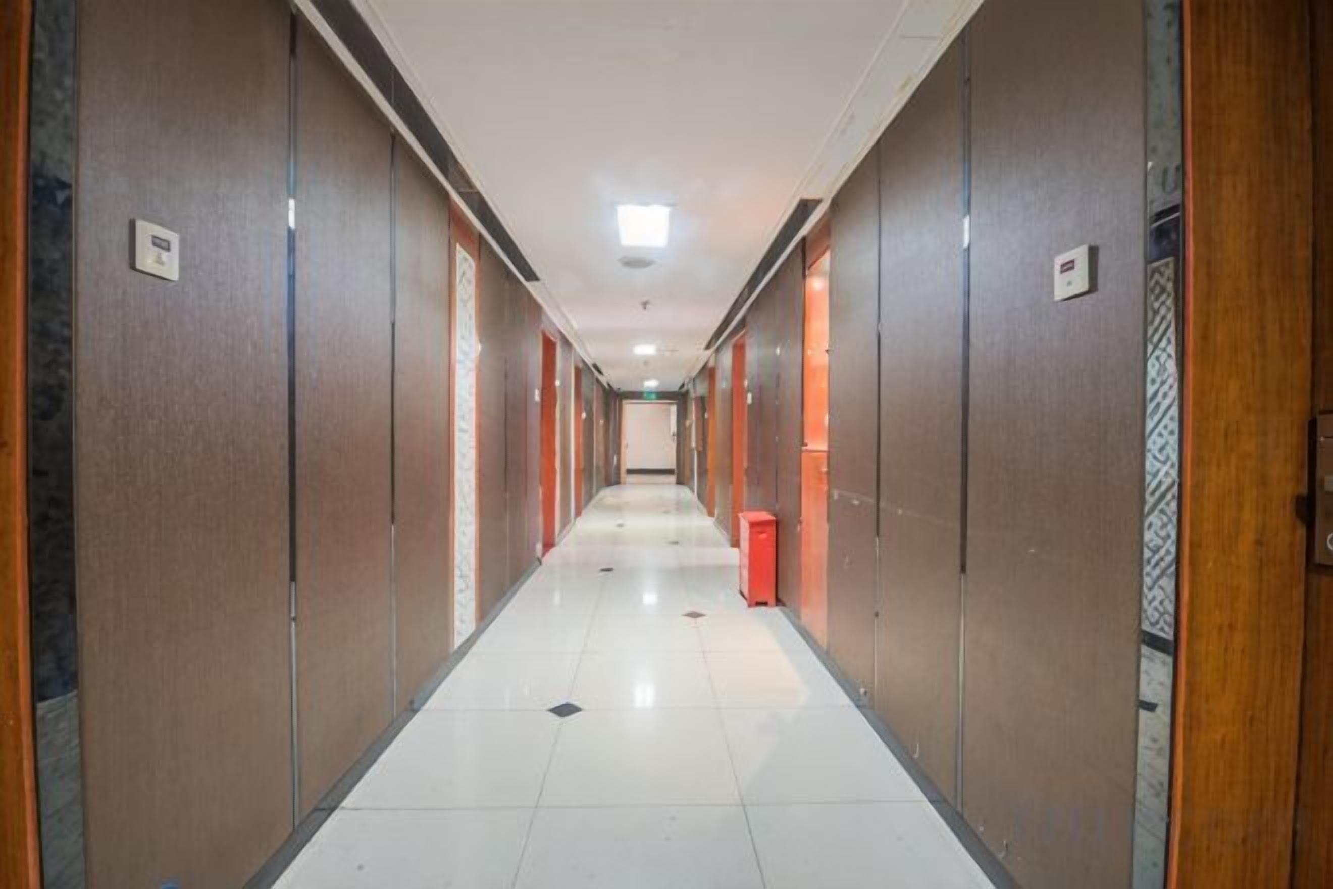 A corridor with doors on both sides, a trash bin, and a light fixture on the ceiling.