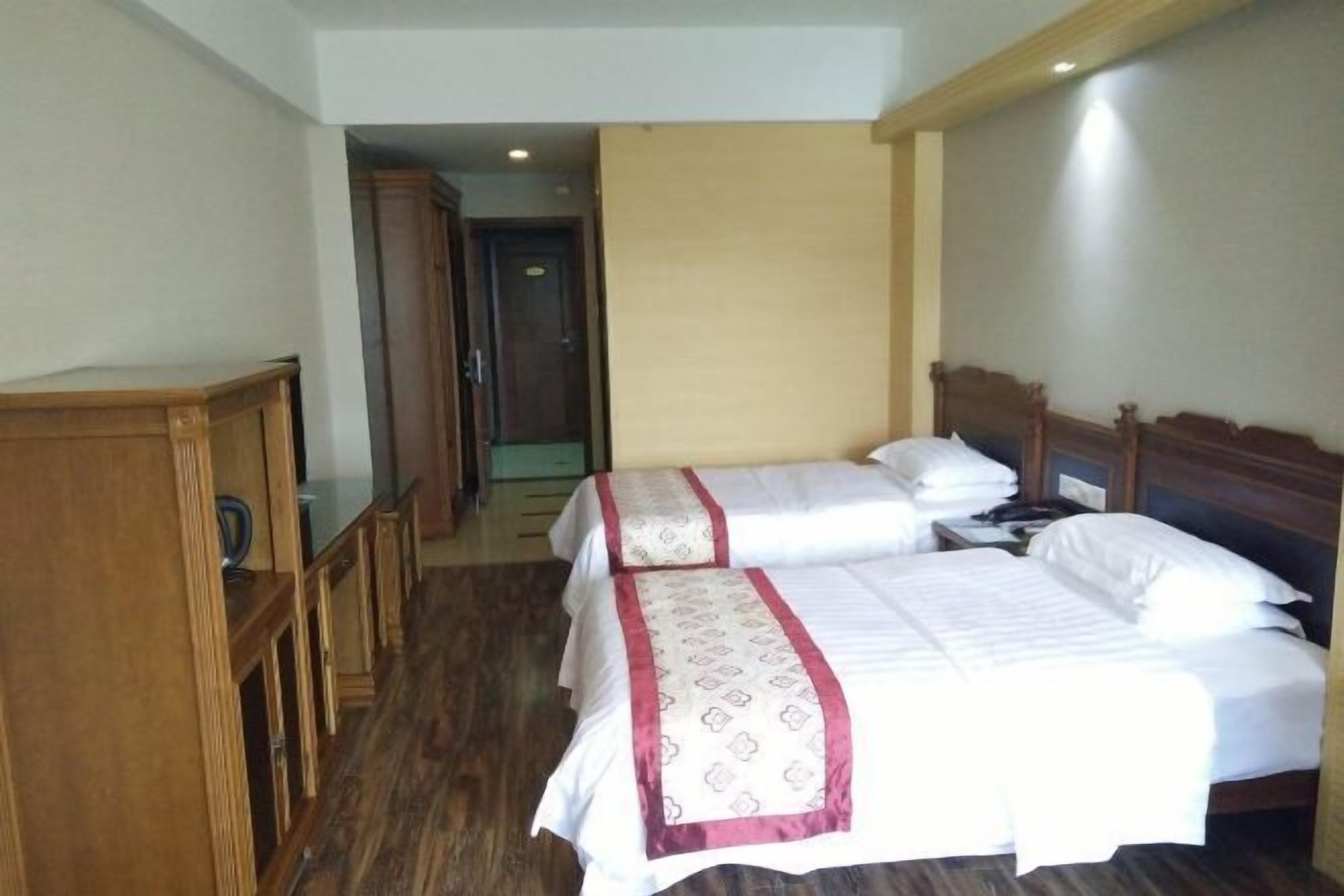 A hotel room with two beds, wooden furniture, and a hallway leading to a door.