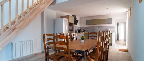 A modern kitchen with a wooden staircase, a dining table with chairs, and a view of the adjacent living area.