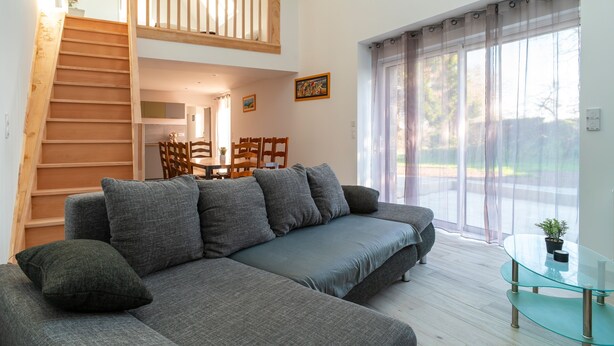A modern living room with a grey sofa, wooden staircase, and a dining area. - Mangoero - Four Bedroom House, Sleeps 12 (Plumergat)