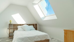 A bedroom with a sloped ceiling, skylights, a wooden bed frame, and a bedside table with a lamp. - Mangoero - Four Bedroom House, Sleeps 12 (Plumergat)