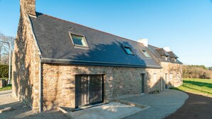 A stone house with a sloped roof, a large sliding glass door, and a small patio area. - Mangoero - Four Bedroom House, Sleeps 12 (Plumergat)