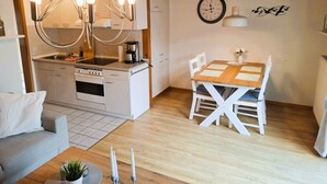 Eine moderne Küche mit einer zentralen Kochinsel, einem Essbereich mit einem Holztisch und weißen Stühlen sowie einem Kronleuchter über der Insel.