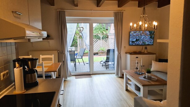 Eine moderne Küche mit Essbereich, einem an der Wand montierten Fernseher und Blick auf den Garten durch Glastüren.
