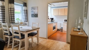 Un comedor con mesa y sillas de madera, una cocina con armarios y electrodomésticos de madera, y vistas al exterior a través de una ventana con cortinas.