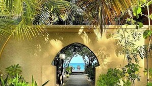 Un sentier menant à une plage, traversant une arche couverte et bordé d’une végétation luxuriante.