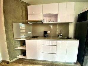 A compact kitchen with white cabinets, a black refrigerator, and a coffee maker.