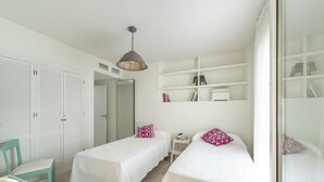 Une chambre avec deux lits simples, une petite table, une chaise, une étagère avec des livres et une armoire.