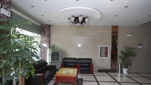 A lobby with a tiled floor, a wooden coffee table, two black sofas, a potted plant, and a ceiling light fixture. - Kunshan Youjian Hotel (Huaqiao Huaxi Park Subway Station) (Kunshan)