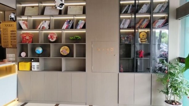 A reception area with a modern design, featuring a grey reception desk, a glass display case with various items, and a potted plant. - Kunshan Youjian Hotel (Huaqiao Huaxi Park Subway Station) (Kunshan)