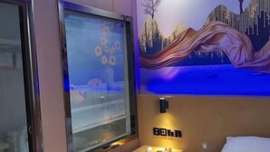 A hotel room with a bed, a bedside table with a lamp, a wall-mounted TV, and a painting of a mountainous landscape. - Kunshan Youjian Hotel (Huaqiao Huaxi Park Subway Station) (Kunshan)
